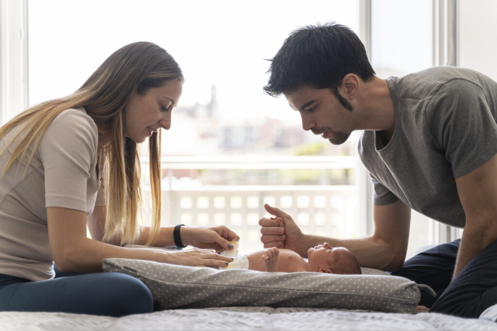 Parents changing their newborn son's diaper on the bed in their bedroom.