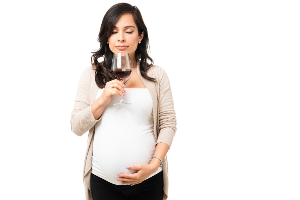 Pregnant woman holding and smelling a glass of wine with her eyes closed.