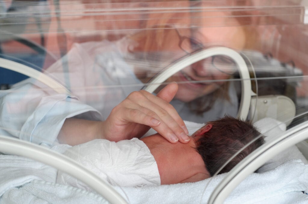 Mother massaging newborn in NICU.